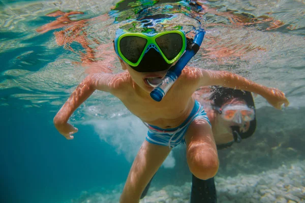 Child learning to snorkel with his mother in sea.