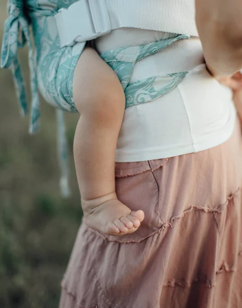 Babybekleidung - Nahaufnahme des nackten Beines eines kleinen Babys, das in einer Tragetasche getragen wird. — Stockfoto