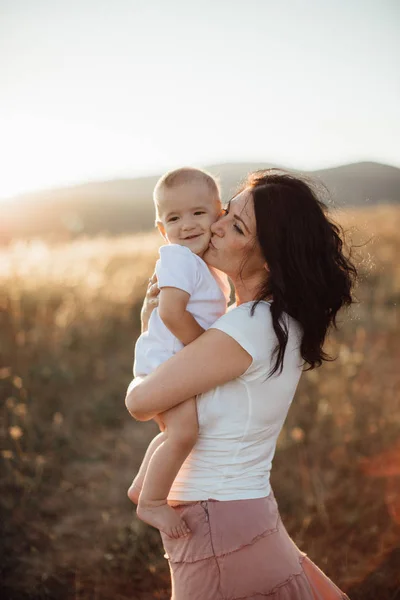 Mutterschaft - junge Mutter umarmt ihr glückliches Baby bei Sonnenuntergang auf den Feldern. — Stockfoto