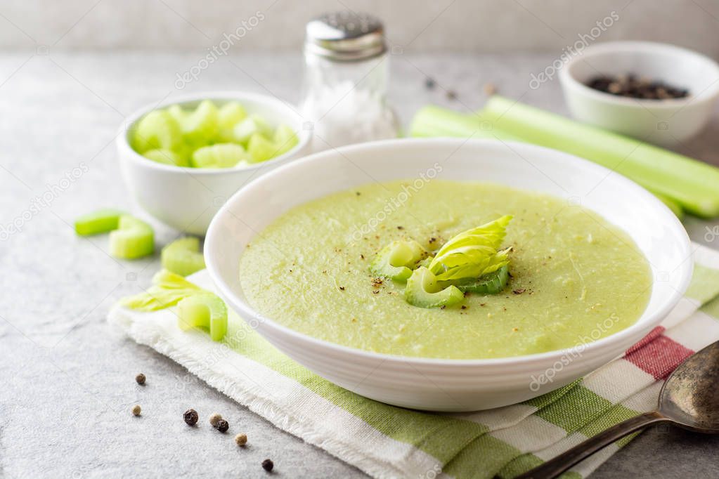 Celery cream soup in white plate on gray stone background. Selective focus.