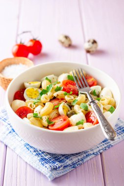 Bıldırcın yumurtası, mozzarella, domates ve mor ahşap zemin üzerine kase Kapari ile makarna salatası. Seçici odak.