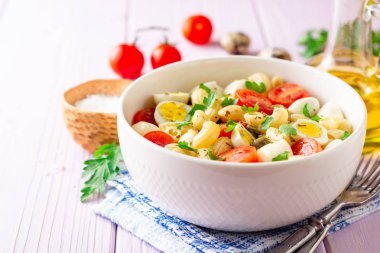 Bıldırcın yumurtası, mozzarella, domates ve mor ahşap zemin üzerine kase Kapari ile makarna salatası. Seçici odak.