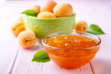 Kayısı reçeli cam kase ve hafif mor ahşap arka plan üzerinde taze kayısı. Seçici odak.