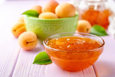 Kayısı reçeli cam kase ve hafif mor ahşap arka plan üzerinde taze kayısı. Seçici odak.