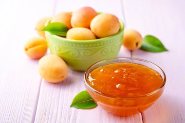 Kayısı reçeli cam kase ve hafif mor ahşap arka plan üzerinde taze kayısı. Seçici odak.