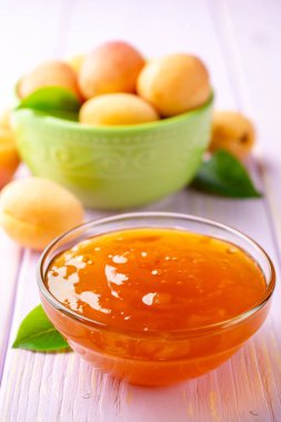 Kayısı reçeli cam kase ve hafif mor ahşap arka plan üzerinde taze kayısı. Seçici odak.