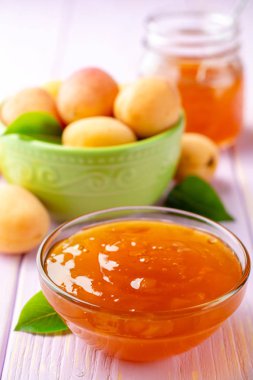 Kayısı reçeli cam kase ve hafif mor ahşap arka plan üzerinde taze kayısı. Seçici odak.