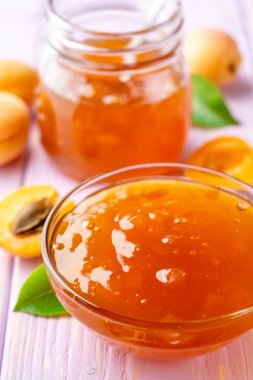 Kayısı reçeli cam kase ve hafif mor ahşap arka plan üzerinde taze kayısı. Seçici odak.