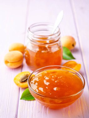 Kayısı reçeli cam kase ve hafif mor ahşap arka plan üzerinde taze kayısı. Seçici odak.