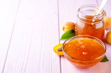 Kayısı reçeli cam kase ve hafif mor ahşap arka plan üzerinde taze kayısı. Seçici odak. Kopya alanı.