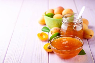 Kayısı reçeli cam kase ve hafif mor ahşap arka plan üzerinde taze kayısı. Seçici odak. Kopya alanı.