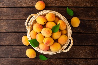 Hasır sepet koyu ahşap zemin üzerine taze kayısı. Üstten görünüm.