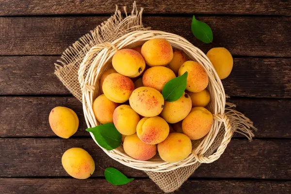 Hasır sepet koyu ahşap zemin üzerine taze kayısı. Üstten görünüm.