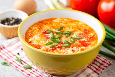 Traditional chinese egg drop soup with tomato and green onion in bowl on gray stone background. Selective focus. clipart
