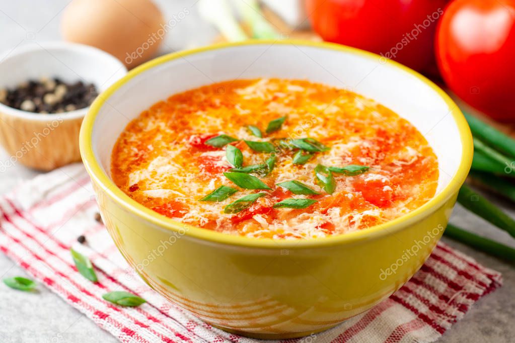 Traditional chinese egg drop soup with tomato and green onion in bowl on gray stone background. Selective focus.