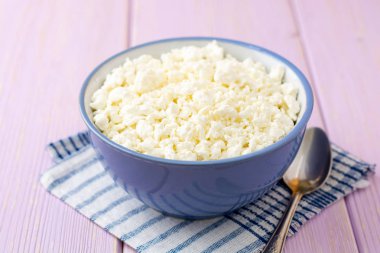 Mor ahşap zemin üzerine mavi kase süzme peynir. Seçici odak.