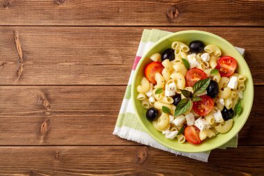 Kiraz domates, siyah zeytin, beyaz peynir ve fesleğen ahşap arka plan ile makarna salatası. Üstten görünüm. Kopya alanı.