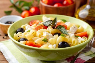 Kiraz domates, siyah zeytin, beyaz peynir ve fesleğen ahşap arka plan ile makarna salatası. Seçici odak.