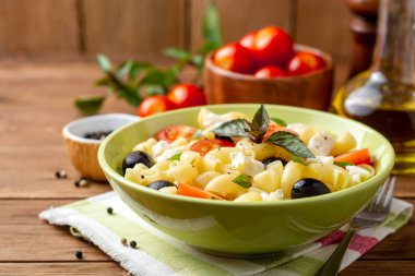 Kiraz domates, siyah zeytin, beyaz peynir ve fesleğen ahşap arka plan ile makarna salatası. Seçici odak.