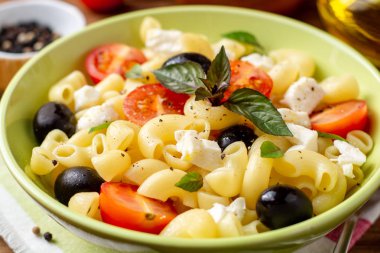 Kiraz domates, siyah zeytin, beyaz peynir ve fesleğen ahşap arka plan ile makarna salatası. Seçici odak.