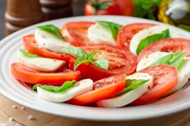 Domates, mozzarella peyniri ve koyu ahşap arka plan tabağa fesleğen ile İtalyan caprese salatası. Seçici odak.