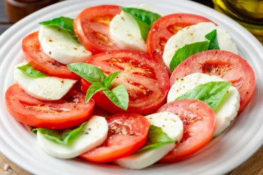 Domates, mozzarella peyniri ve koyu ahşap arka plan tabağa fesleğen ile İtalyan caprese salatası. Seçici odak.