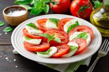 Domates, mozzarella peyniri ve koyu ahşap arka plan tabağa fesleğen ile İtalyan caprese salatası. Seçici odak.