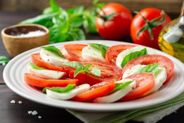 Domates, mozzarella peyniri ve koyu ahşap arka plan tabağa fesleğen ile İtalyan caprese salatası. Seçici odak.