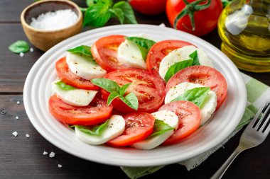 Domates, mozzarella peyniri ve koyu ahşap arka plan tabağa fesleğen ile İtalyan caprese salatası. Seçici odak.