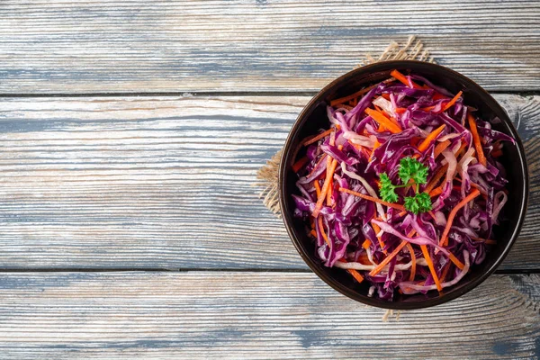 Fresh coleslaw salad with red and white cabbage and carrots in bowl on vintage wooden background. Top view. Copy space.