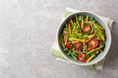 Kuşkonmaz, biber, domates, kırmızı soğan ve seramik kase taş zemin üzerine yeşil bezelye salatası. Üstten görünüm. Kopya alanı.