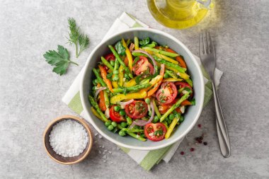 Kuşkonmaz, biber, domates, kırmızı soğan ve seramik kase taş zemin üzerine yeşil bezelye salatası. Üstten görünüm.