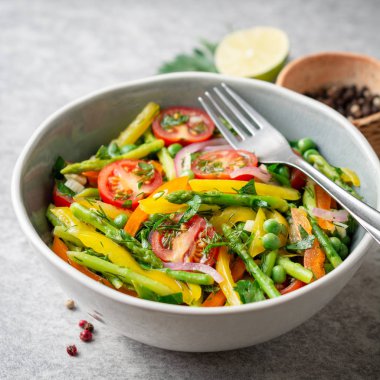 Kuşkonmaz, biber, domates, kırmızı soğan ve seramik kase taş zemin üzerine yeşil bezelye salatası. Seçici odak.