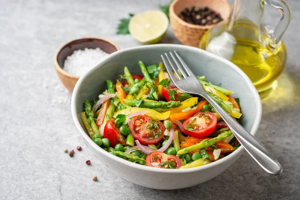 Kuşkonmaz, biber, domates, kırmızı soğan ve seramik kase taş zemin üzerine yeşil bezelye salatası. Seçici odak.