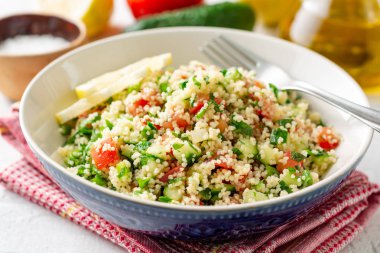 Beton arka plan üzerinde kuskus, sebze ve yeşillik ile Geleneksel Arap Salatası Tabbouleh. Seçici odaklama.