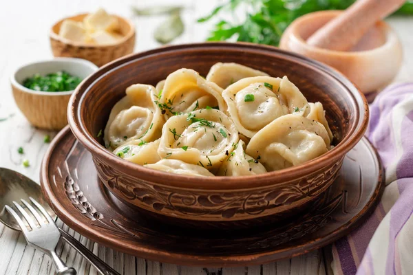 Beyaz ahşap masa üzerinde seramik kase tereyağı ve yeşillik ile geleneksel Rus ev yapımı et köfte pelmeni. Seçici odaklama.