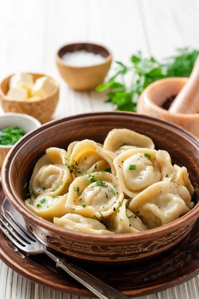 Beyaz ahşap masa üzerinde seramik kase tereyağı ve yeşillik ile geleneksel Rus ev yapımı et köfte pelmeni. Seçici odaklama.