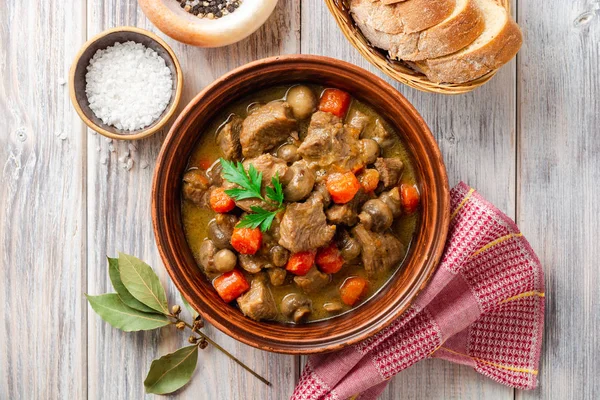 Turkey meat stew with mushrooms and vegetables in ceramic bowl on wooden table. Top view.