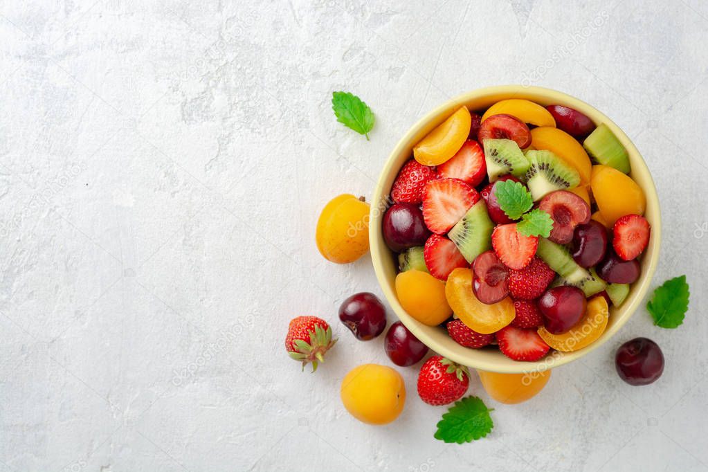 Healthy fresh fruit salad in bowl on gray concrete background. Top view. Copy space.