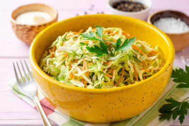 Mor ahşap arka planda kase lahana, havuç ve salatalık ile coleslaw salata. Seçici odak.