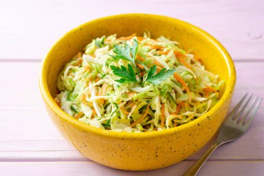 Mor ahşap arka planda kase lahana, havuç ve salatalık ile coleslaw salata. Seçici odak.