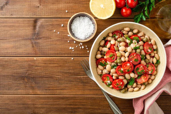 Ensalada de frijoles blancos con tomates, alcaparras, ajo y perejil en tazón sobre mesa de madera — Foto de Stock