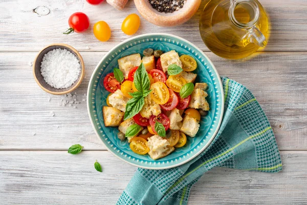 Geleneksel Italyan salata Panzanella kiraz domates, ekmek, kapanlar ve ahşap masada kase fesleğen. Üst görünüm.
