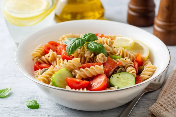 Whole wheat pasta salad with cucumbers, cherry tomatoes, salted salmon and capers on concrete background. Selective focus.