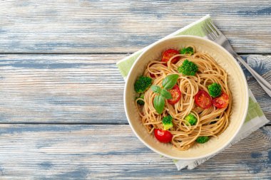 Brokoli, kiraz domates ve fesleğen ahşap arka planda kase ile kepekli spagetti makarna. Üst te. Kopyalama alanı.