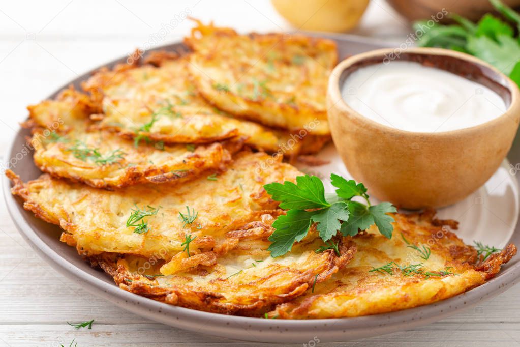 Potato pancakes or latkes or draniki with sour cream in plate on white wooden table. Selective focus.