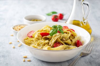 Sos soslu Fettuccine makarna, kiraz domatesleri, çam fıstığı ve çimento arka planda parmesan peyniri. Seçici odak.