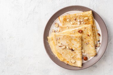 Beyaz beton arka planda fındıklı krep ve pudra şekeri. Üst Manzara. Boşluğu kopyala.