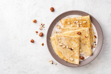 Beyaz beton arka planda fındıklı krep ve pudra şekeri. Üst Manzara. Boşluğu kopyala.