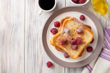 Pudra şekerli yumurtalı ekmek ve ahşap masada taze ahududu. Üst Manzara. Boşluğu kopyala.